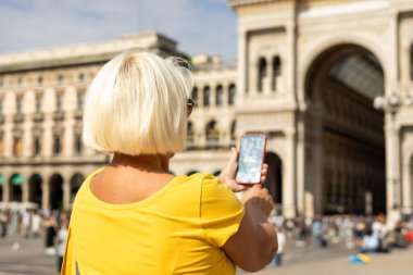 Sokakta oturan ve telefonu tutan son sınıf güzeli bir kadın. Turist Duomo Meydanı 'ndaki akıllı telefonunu kontrol ediyor. Galleria Vittorio Emanuele II..