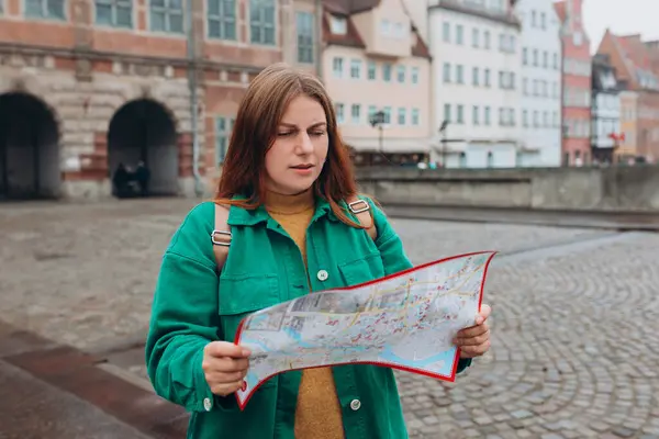 Portrait beautiful woman with paper map on urban street. Young worried female traveler lost in the city using map. Vacation concept by exploring new places to travel.