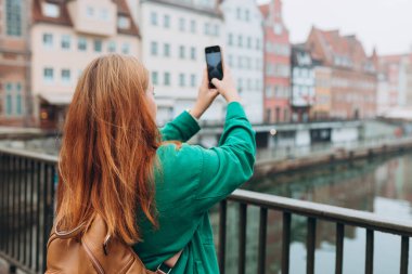 Genç Avrupalı turist, Polonya 'nın Gdansk kentindeki akıllı telefondan fotoğraf veya video çekiyor. Sırt çantalı hippi kız akıllı telefon aletini tut.
