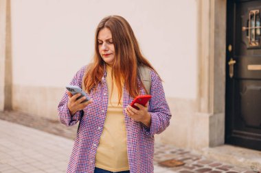 Şehir caddesinde iki telefonu olan üzgün ve sinirli bir kız. Negatif insanların duyguları. Üzgün 30 'lu yaşlardaki genç bir kadın açık havada akıllı telefon kullanıyor.