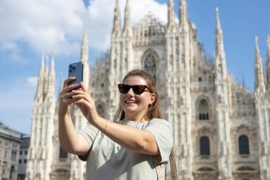 Genç ve mutlu bir turist Milano 'daki ünlü Duomo katedralinin önünde selfie çekiyor. Yazın Avrupa 'yı geziyorum. Çekici kadın şehri keşfediyor, turist telefonla fotoğraf ya da video çekiyor