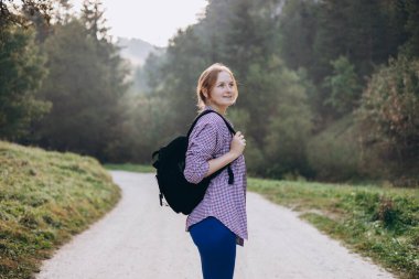 Sırt çantalı genç bir kadın doğa yolunda yürüyüş yapıyor. 30 'lu yaşlardaki güzel bir kadın ormanda koşu kıyafetleriyle yürüyor. Seyahat konsepti, atmosferik an.