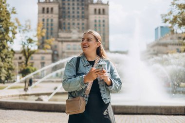 Polonya 'nın Varşova şehrindeki Kültür ve Bilim Sarayı yakınlarındaki parkta yürüyen genç bir turist. Dışarıda dinlenirken cep telefonuyla konuşan bir kadın. Teknoloji, Kentsel yaşam tarzı konsepti