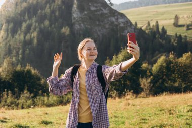Kadın fotoğraf çekmek için telefon kullanıyor. Dağların arka planında evden arkadaşları ve aileleriyle fotoğraf çekiyor. Seyahat ve seyahat tutkusu konsepti. İnanılmaz soğuk bir an.