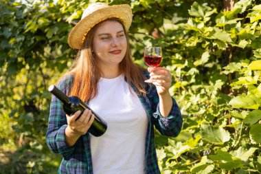 Üzüm bağında kırmızı şarap içen bir kadın. Elinde bir kadeh şarap ve bir şişe şarap tutan güzel genç bir kadının portresi. Tasarım için model