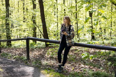 Akıllı telefonlu mutlu genç bir kadın ormanda yürürken siyah bir sırt çantası takıyor. Bahar geldi. 30 'lu yaşlarda ormanda yürüyüş yapan spor elbiseli kadınlar. Seyahat konsepti