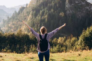 Dağ zirvesinde sırt çantalı bir kadın yürüyüşçü. Seyahat ve aktif yaşam tarzı konsepti. Otuzlu yaşların kızı dağın tepesinden vadi manzarasını seyrediyor, açık hava aktivitelerini.