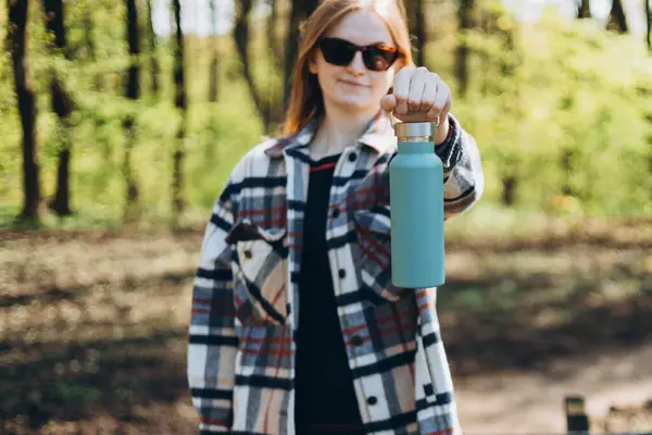 Happy Woman in sport clothes having a halt after hiking. Hiker drinking water from water bottle or hot drink from blue thermos