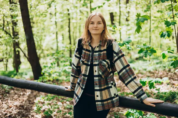 Günlük kıyafetli genç bir kadın, ormanda yürürken siyah bir sırt çantası takıyor. Bahar geldi. 30 'lu yaşlarda ormanda yürüyüş yapan spor elbiseli kadınlar.