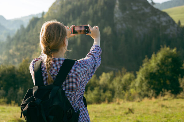 Tourist on top of the mountain takes a photo. Woman traveler takes a photo on a modern smartphone, makes beautiful pictures of beautiful mountain landscapes.