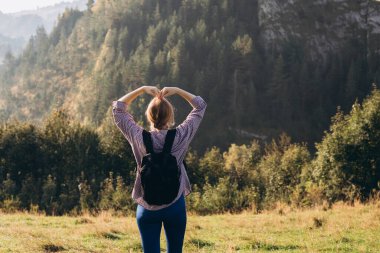Sırt çantalı, ormanda yürüyüş yapan şık bir kadının arka görüntüsü. Özgürlük ve aktif yaşam tarzı kavramı. Aşk dolu kalp şeklinde eller yapan maceraperest kadınlar.