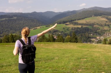 Dağ zirvesinde sırt çantalı, kolları açık bir kadın yürüyüşçü. Seyahat ve aktif yaşam tarzı konsepti. 30 'lu yaşların kızı dağın tepesinden vadi manzarasını, açık hava aktivitelerini, dikiz manzarasını seviyor.