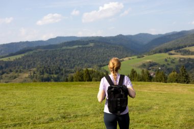 Otuzlu yaşların kızı dağ zirvesinde yeşil çimlerle kaplı sırt çantasıyla yazın gün batımında sisli dağ vadisine bakıyor. Sportif genç bayanla manzara