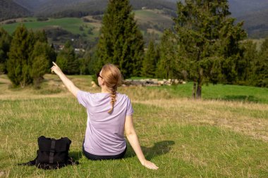 Aktif yürüyüş kıyafetleri içindeki bir kadının yürüyüş sonrası duruşu. Seyahat ve aktif yaşam tarzı konsepti. Otuzlu yaşların kızı bir dağın tepesinden vadi manzarasının keyfini çıkarıyor.