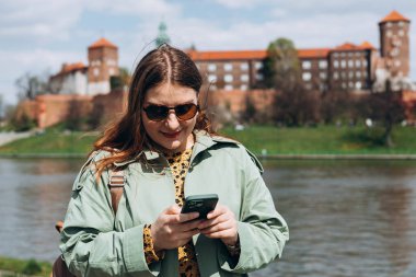 Güzel, şık bir kadın bahar günü yürüyor ve arka planda cep telefonu tutuyor. Telefon iletişimi. Şehir yaşam tarzı konsepti. Sosyal ağları kontrol et