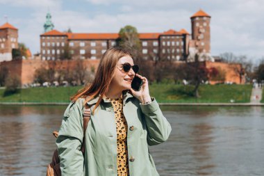 Şehir caddesinden akıllı telefonlu mutlu genç bir kadın arıyor. Teknoloji, iletişim ve insan konsepti. 30 'lu yaşlardaki pozitif kadın şehir geçmişi ve eski kasaba hakkında konuşuyor.