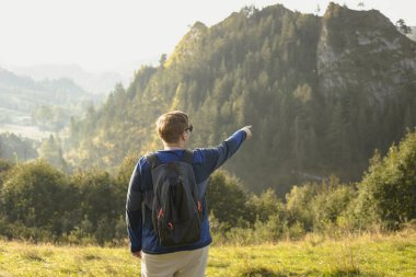 Erkekler dağları işaret ediyor. Sırt çantasıyla doğa yürüyüşü yapan genç bir erkek..