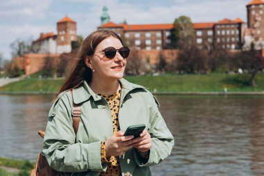 Güzel, şık bir kadın bahar günü yürüyor ve arka planda cep telefonu tutuyor. Telefon iletişimi. Şehir yaşam tarzı konsepti. Sosyal ağları kontrol et