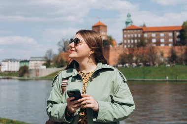 Güzel, şık bir kadın bahar günü yürüyor ve arka planda cep telefonu tutuyor. Telefon iletişimi. Şehir yaşam tarzı konsepti. Sosyal ağları kontrol et