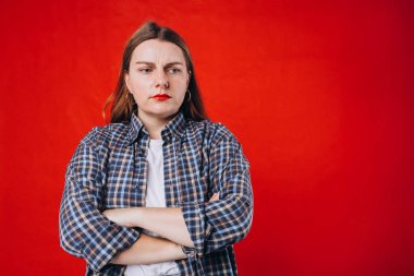 Kızgın genç kadın kırmızı arka planda tek başına duruyor. Duygusal, genç yüz. İnsani duygular, yüz ifadesi kavramı.