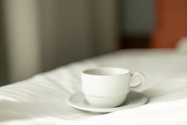 Coffee or tea cup on the bed. Hotel room or bedroom Interior, morning time. Concept of easy breakfast. One white big ceramic cup.