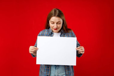 30 'lu yaşlardaki güzel bir kadın elinde boş bir reklam pankartı tutuyor. Kırmızı arka planda izole edilmiş..