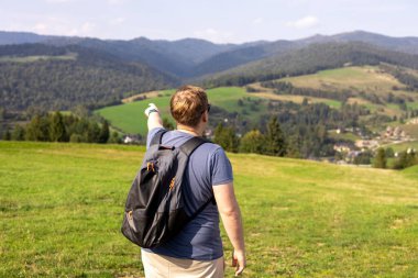 Erkekler dağları işaret ediyor. Sırt çantalı, doğa yürüyüşü yapan genç bir erkek. Arka plan