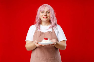 Fırıncı önlüklü beyaz tişörtlü, elinde pastayla stüdyoda kırmızı arka planda izole bir tabak tutuyor. Yiyecek konsepti