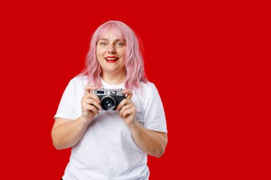 Kırmızı arka planda fotoğraf makinesi olan gülümseyen genç bir kadının portresi.