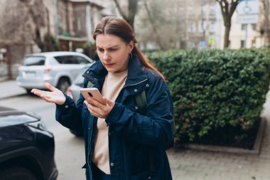 Üzgün, kuşkucu, ciddi bir kadın dışarıda iletişim kurmak için akıllı telefon aleti tutuyor. Negatif insan duyguları, şehir yaşam tarzı konsepti. Kızgın 30 'lu yaşlardaki kız kötü haber okuyor.