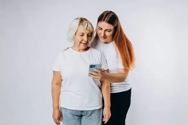 stock image Happy cool elder parent mom with young adult daughter two women together wear casual clothes hold in hand use mobile cell phone isolated on white background. Family day concept