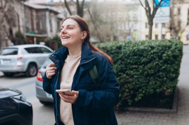 Sırt çantalı mutlu genç kadın akıllı telefonunu kontrol ediyor. Açık havada akıllı telefon kullanan 30 'lu yaşlardaki güzel bir kızın portresi. Şehir ya da teknoloji kavramı.