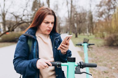 Kafası karışmış bir kadının portresi, elinde akıllı telefon, şehir arka planında mobil uygulama kullanıyor.