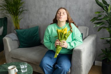 Bir kadın elinde buketle evdeki kanepede, otelde oturuyor. 30 'lu yaşlarda kadın dinleniyor ve oturma odasında boş zaman geçiriyor. İnsanlar dinlenir ya da tatil konsepti