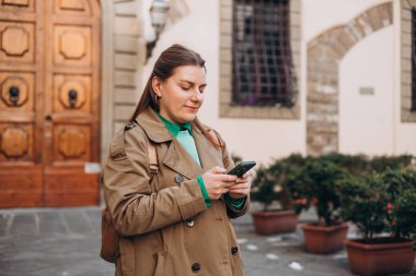 Sırt çantalı mutlu genç kadın akıllı telefonunu kontrol ediyor. Açık havada akıllı telefon kullanan 30 'lu yaşlardaki güzel bir kızın portresi. Bahar geldi.