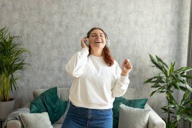 Evdeki oturma odasında şarkı söyleyip dans eden 30 'lu yaşlarında mutlu bir kadın. Bağımsız kadın portresi. Ev yaşamında yalnızım.