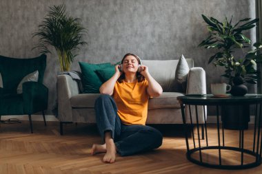 Gülümseyen kız evde dinleniyor, akıllı telefon kullanarak müzik çalıyor ve beyaz kulaklık takıyor. Genç bir kadın evdeki kanepede iyi ses sesinden zevk alıyor..