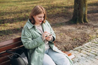 Sıradan giyinmiş 30 'lu yaşlardaki neşeli turist şehir sokaklarında iletişim kurmak için elinde akıllı telefon aleti tutuyor. Mutlu kadın cep telefonuyla konuşuyor ve dışarıda bankta dinleniyor.