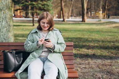 Sıradan giyinmiş 30 'lu yaşlardaki neşeli turist şehir sokaklarında iletişim kurmak için elinde akıllı telefon aleti tutuyor. Mutlu kadın cep telefonuyla konuşuyor ve dışarıda bankta dinleniyor.