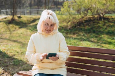 Zarif, olgun bir kadın dışarıda oturuyor ve elinde şehir sokaklarında iletişim kurmak için akıllı telefon aleti tutuyor. Kentsel, halk konsepti.