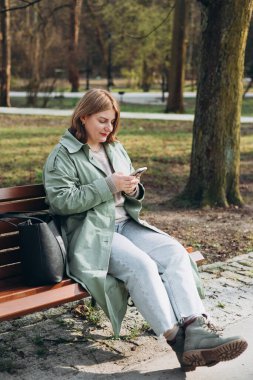 Sıradan giyinmiş 30 'lu yaşlardaki neşeli turist şehir sokaklarında iletişim kurmak için elinde akıllı telefon aleti tutuyor. Mutlu kadın cep telefonuyla konuşuyor ve dışarıda bankta dinleniyor.