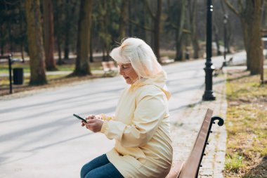 Zarif, olgun bir kadın dışarıda oturuyor ve elinde şehir sokaklarında iletişim kurmak için akıllı telefon aleti tutuyor. Kentsel, halk konsepti.