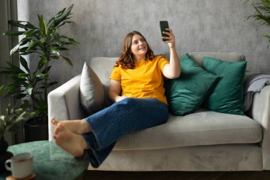 - Selam. Esmer kadın cep telefonuyla kendi fotoğrafını çekiyor. 30 'lu yaşlardaki kadın kendini videoya kaydediyor, internette konuşuyor ve kanepede dinleniyor. Tüm vücut