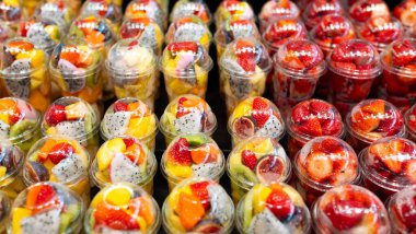 Markette plastik bardaklara yerleştirilmiş meyve salatası. Piyasada satılmaya hazır meyveler. Uygun, sağlıklı bir yaşam tarzı. Çilek, kivi, kavun, ananas, incir, plastik bardaktaki ejderha.