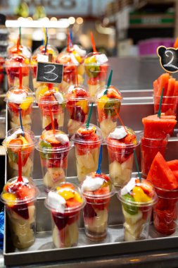 Markette plastik bardaklara yerleştirilmiş meyve salatası. Piyasada satılmaya hazır meyveler. Uygun, sağlıklı bir yaşam tarzı. Çilek, kivi, kavun, ananas, incir, plastik bardaktaki ejderha.