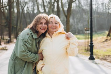 Mutlu olgun anne ve kız gülüyor, şefkatli genç bir kadın sarılıyor orta yaşlı anneyi kucaklıyor doğayla iç içe vakit geçiriyorlar. Aile Günü