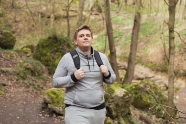 Sırt çantalı genç bir erkek doğa yolunda yürüyüş yapıyor. 30 'lu yaşlardaki spor elbiseli adamlar ormanlık alanda yürüyor. Erkek portresi yaşam tarzı.