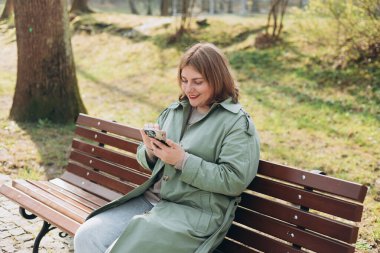 Sıradan giyinmiş 30 'lu yaşlardaki neşeli turist şehir sokaklarında iletişim kurmak için elinde akıllı telefon aleti tutuyor. Mutlu kadın cep telefonuyla konuşuyor ve dışarıda bankta dinleniyor.