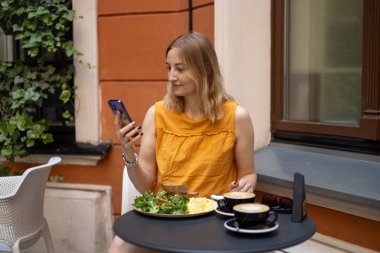 30 'lu yaşlardaki güzel bir kızın portresi bir kafede içiyor, kahve içiyor, mutlu duygular içinde. Gülümseyen ve kafede akıllı telefon kullanan genç ve mutlu bir kadın. Telefon İletişimi.