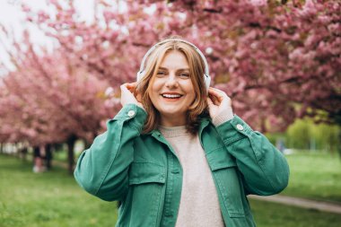 Parkta müzik dinleyen 30 'lu yaşlarda, kocaman kulaklıklı çekici bir kadının portresi. Müzik aşığı müziğin tadını çıkarıyor. Sakura 'nın çiçek açan bir dalıyla bahar arkaplanı.